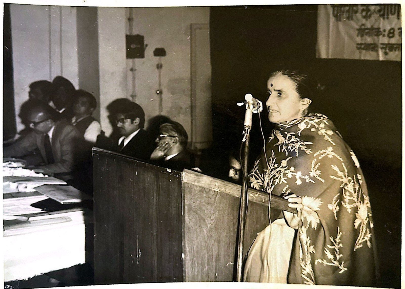 Dr. Rameshwari Sethi speaking at a podium before a seated panel, beneath a family welfare banner